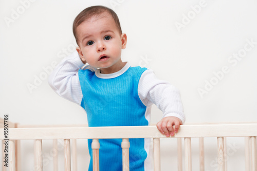 Adorable baby toddler look at camera in the bed with hand on head on white background