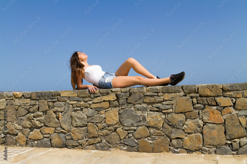 Fototapeta premium Young beautiful brunette in jean shorts enjoys the summer sun