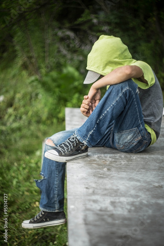 Bild auf Leinwand a homeless boy sits on a bench with her head bowed down
