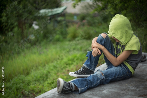 a homeless boy sits on a bench with her head bowed down photo