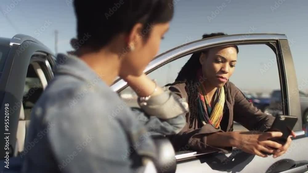 Girlfriends leaning against car at the beach talking and texting with cellphones