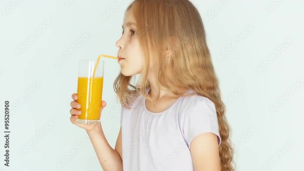 Girl drinking orange juice and smiling at camera. Girl with beautiful blonde hair on a white background. Child nods. Thumb up. Ok. Closeup Girl drinking orange juice and smiling at camera. Girl with beautiful blonde hair on a white background. Child nods. Thumb up. Ok. Closeup