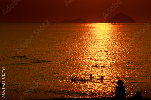 people swim in sea among sun reflection at sunrise