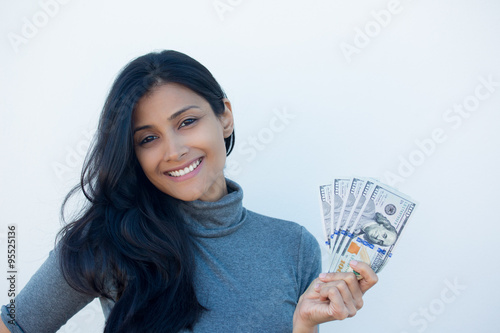 Closeup portrait, excited successful young business woman in gray shirt holding money dollar bills in hand, isolated white wall background. Positive emotion facial expression feeling. Financial reward