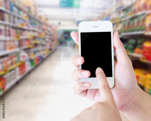 hand holding mobile phone with supermarket shelves aisle blurred