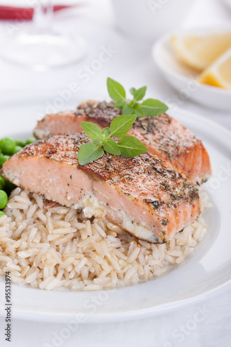 Baked salmon with rice, green peas and basil on a white ceramic plate on a white background.