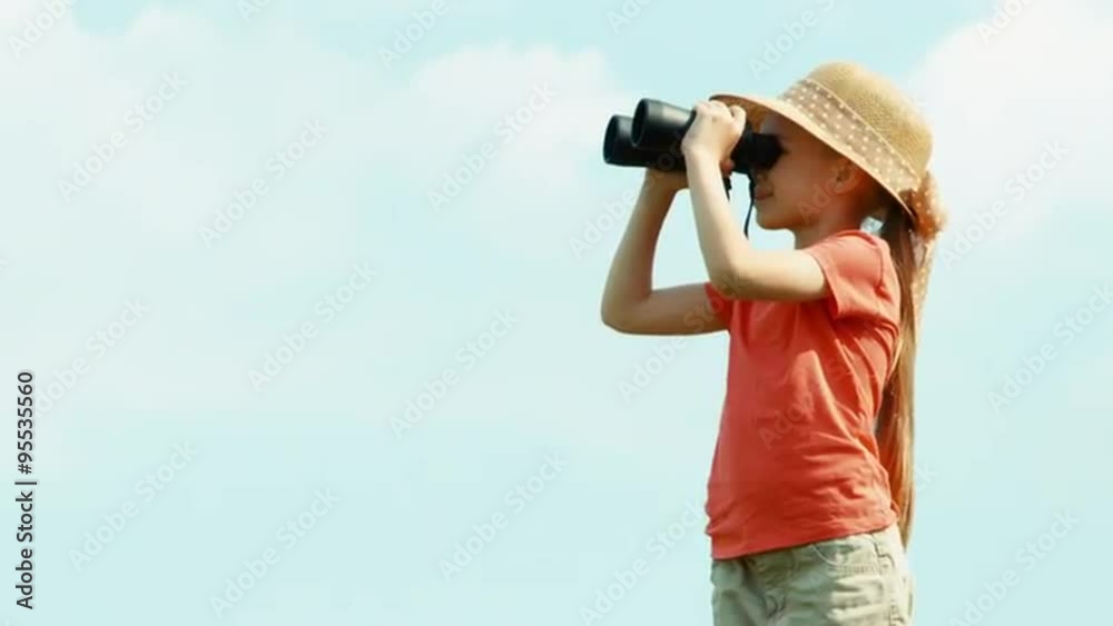 Girl through binoculars watching wildlife. Girl standing against the sky and waving hand Girl through binoculars watching wildlife. Girl standing against the sky and waving hand