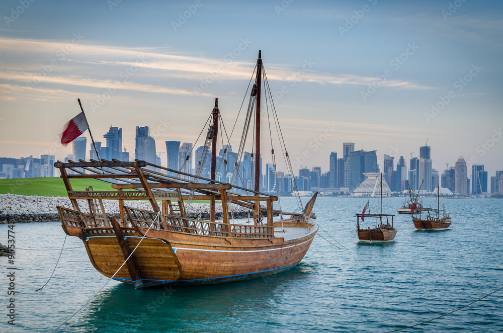Obraz premium Dhows moored off Museum Park in central Doha, Qatar, Arabia, with some of the buildings from the city's commercial port in the background.