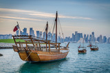 Dhows moored off Museum Park in central Doha, Qatar, Arabia, with some of the buildings from the city's commercial port in the background.