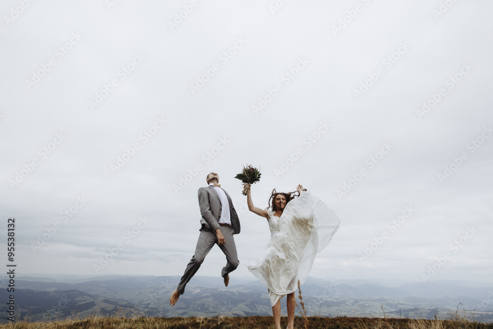 Obraz premium beautiful fabulous happy bride and stylish groom jumping on th