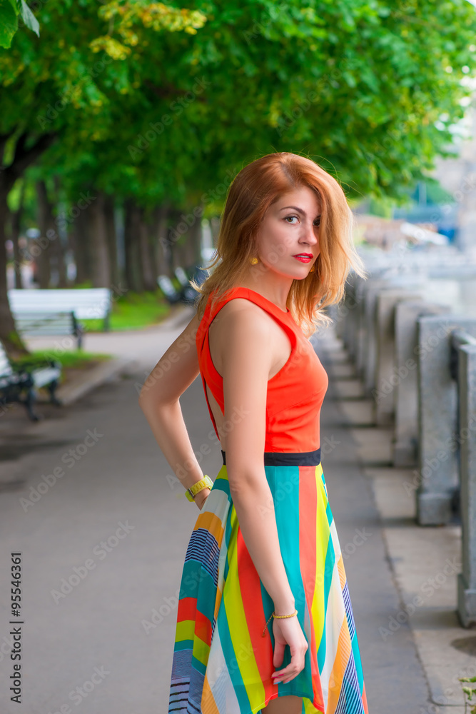 young beautiful girl walks on the waterfront in a bright dress