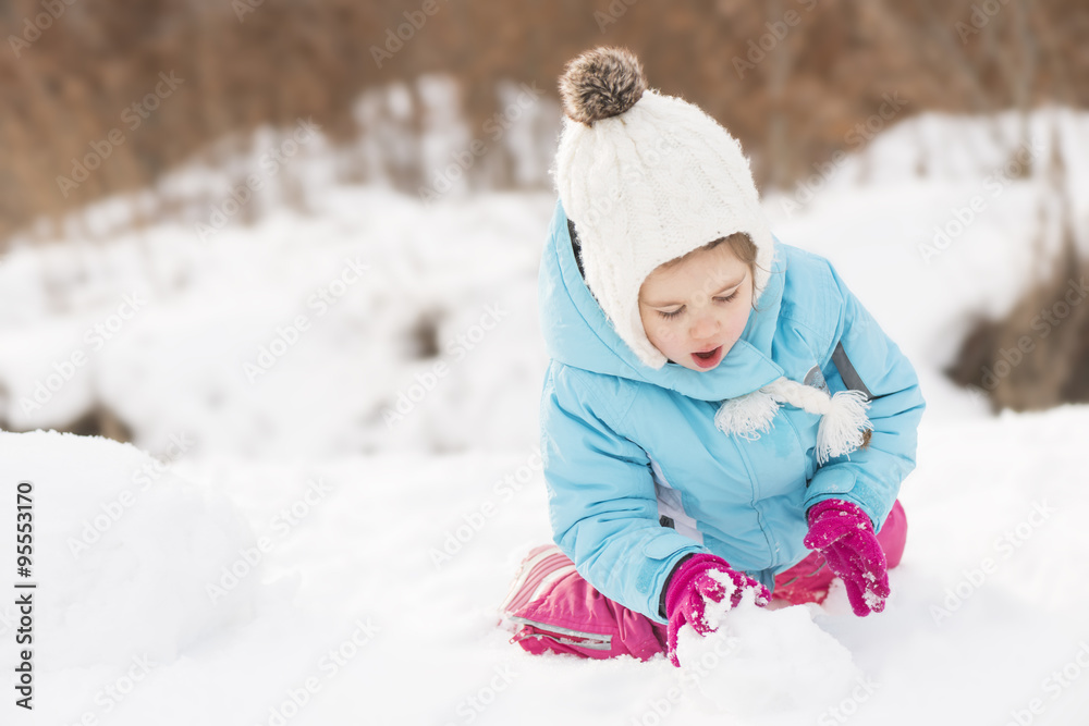 Funny little girl in a warm winter outfit, building a snow man. Kid playing outdoors in winter. Happy little kid is playing in snow, good winter weather Funny little girl in a warm winter outfit, building a snow man. Kid playing outdoors in winter. Happy little kid is playing in snow, good winter weather