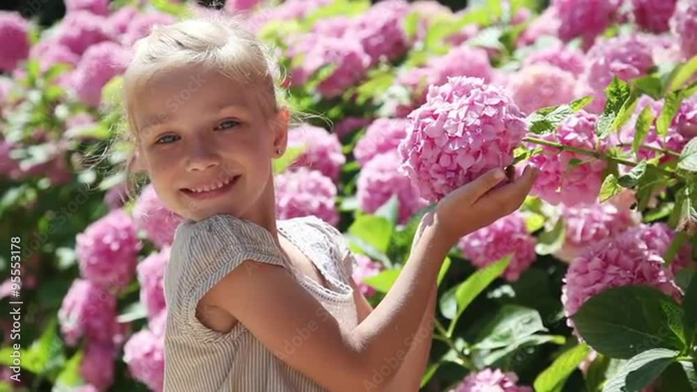Happy little girl smelling a flower and smiling at the camera