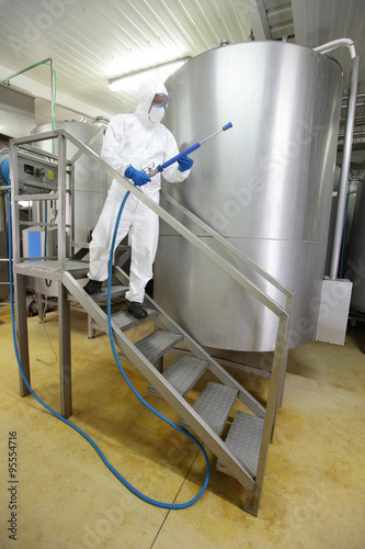 worker in white protective uniform with  high pressure washer on stairs at large industrial process tank preparing to cleaning photo