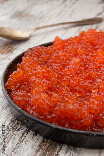 Red caviar in a black plate over a vintage background