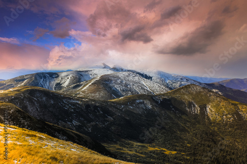 Autumn landscape in the snowy top mountains and majestic clouds in the evening sky.