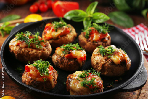 A frying pan with stuffed mushrooms and vegetables on the table