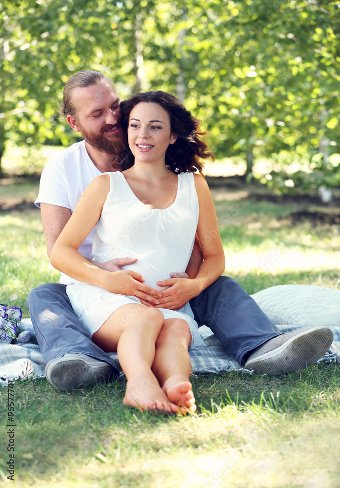 Happy couple embrace sitting on white blanket in the park Happy couple embrace sitting on white blanket in the park