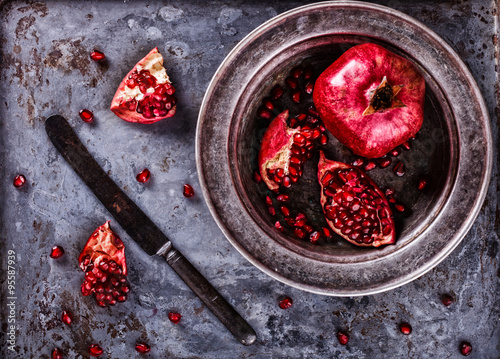 Juicy pomegranates,whole and broken vintageon a metal plate.Toned image. Vintage styleselective focus. photo