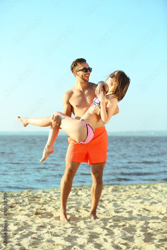 A guy holding a girl in the arms, at the beach, outdoors