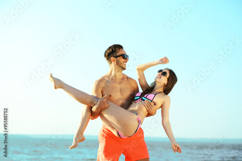 A guy holding a girl in the arms, at the beach, outdoors © Africa Studio