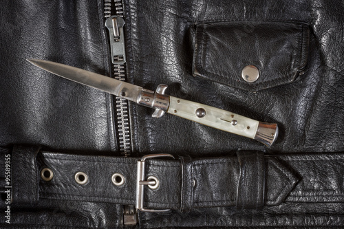 Canvas Print Opened flick knife on a black leather jacket with zip, belt and pocket
