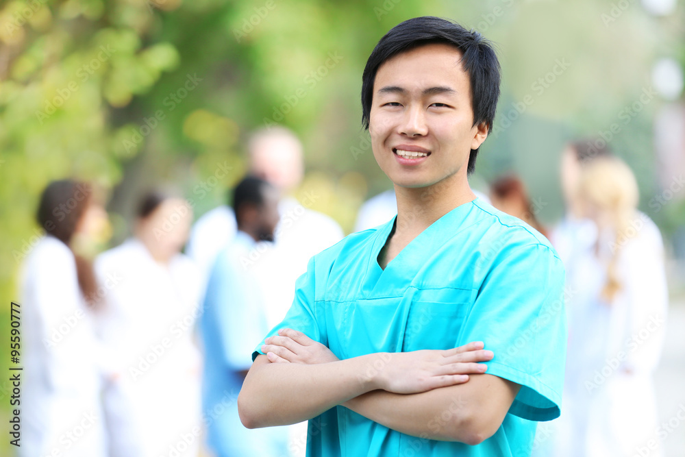 Young smiling doctor standing against unfocused group of medical workers Young smiling doctor standing against unfocused group of medical workers