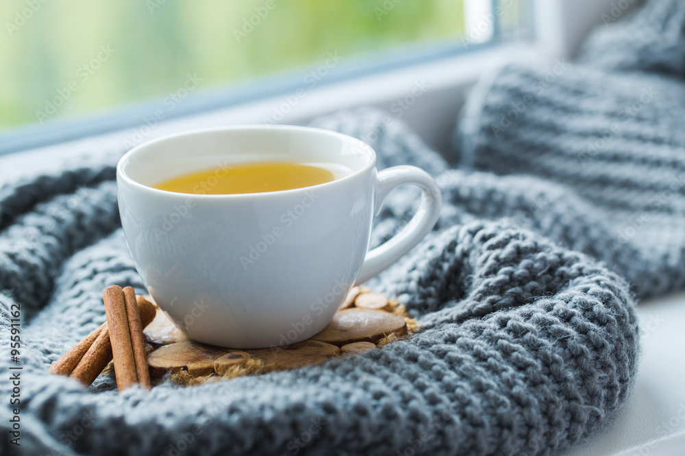 White cup of chamomile tea with grey scarf on the windowsill.