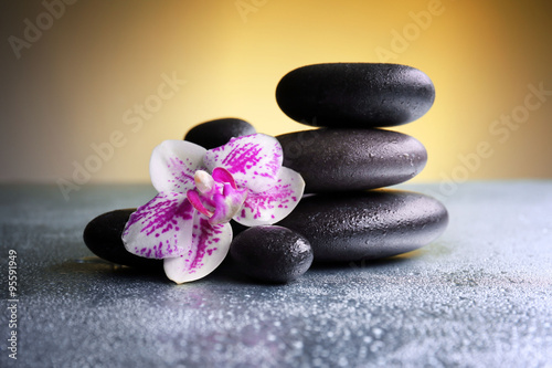 Black pebbles with orchid on grey table, close up