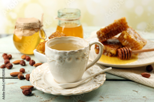 Honeycomb, bowl with honey, cup with herbal tea on color wooden table, on light background