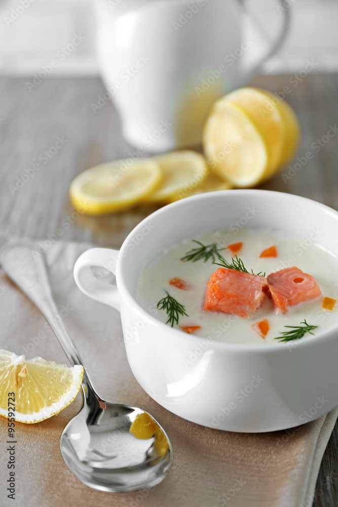 Delicious salmon cream soup on wooden table, which served with sliced lemon and spices Delicious salmon cream soup on wooden table, which served with sliced lemon and spices