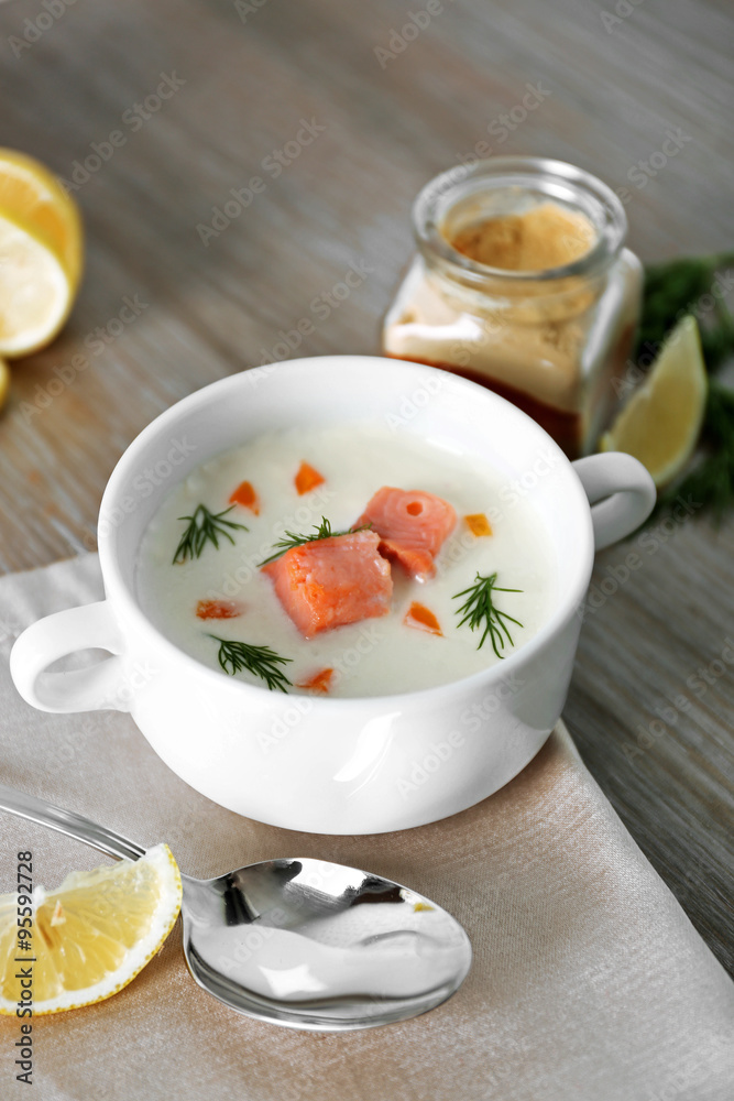Delicious salmon cream soup on wooden table, which served with sliced lemon and spices Delicious salmon cream soup on wooden table, which served with sliced lemon and spices