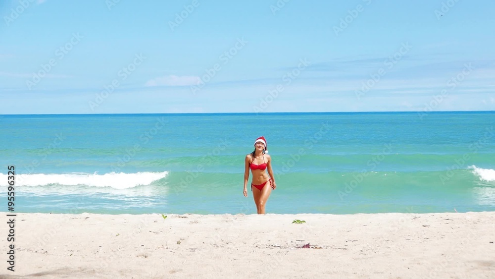 Beautiful Caucasian christmas woman in santa hat and red bikini jokes and relaxing on the beach with white sand. New Year in jungle sea view and sunlight. Holiday in tropics. Beautiful Caucasian christmas woman in santa hat and red bikini jokes and relaxing on the beach with white sand. New Year in jungle sea view and sunlight. Holiday in tropics.