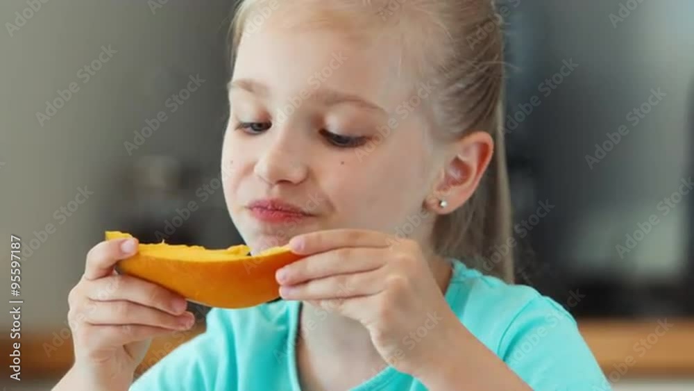 Closeup portrait girl eating mango. Child sitting at the kitchen table and looking at camera Closeup portrait girl eating mango. Child sitting at the kitchen table and looking at camera