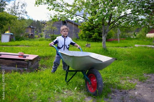 Cute young baby boy pushing wheelbarrow in garden photo