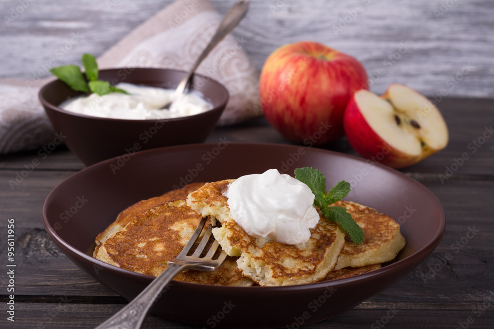 Cottage cheese pancake with apples in ceramic bowl with sour cream on a dark wooden table