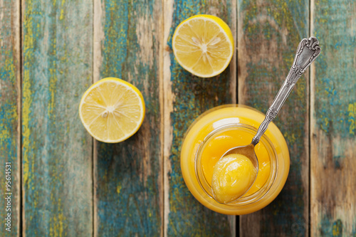 Lemon curd in glass jar on rustic wooden table, traditional fruit cream, vintage style, top view photo