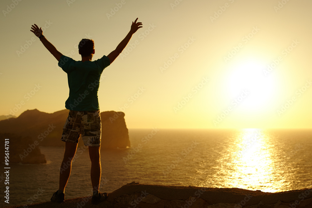 Fototapeta premium Silhouette of a young man with hands raised in the sunset. Cocept on winner. Success. Explorer. Man at Cap Formentor, Majorca