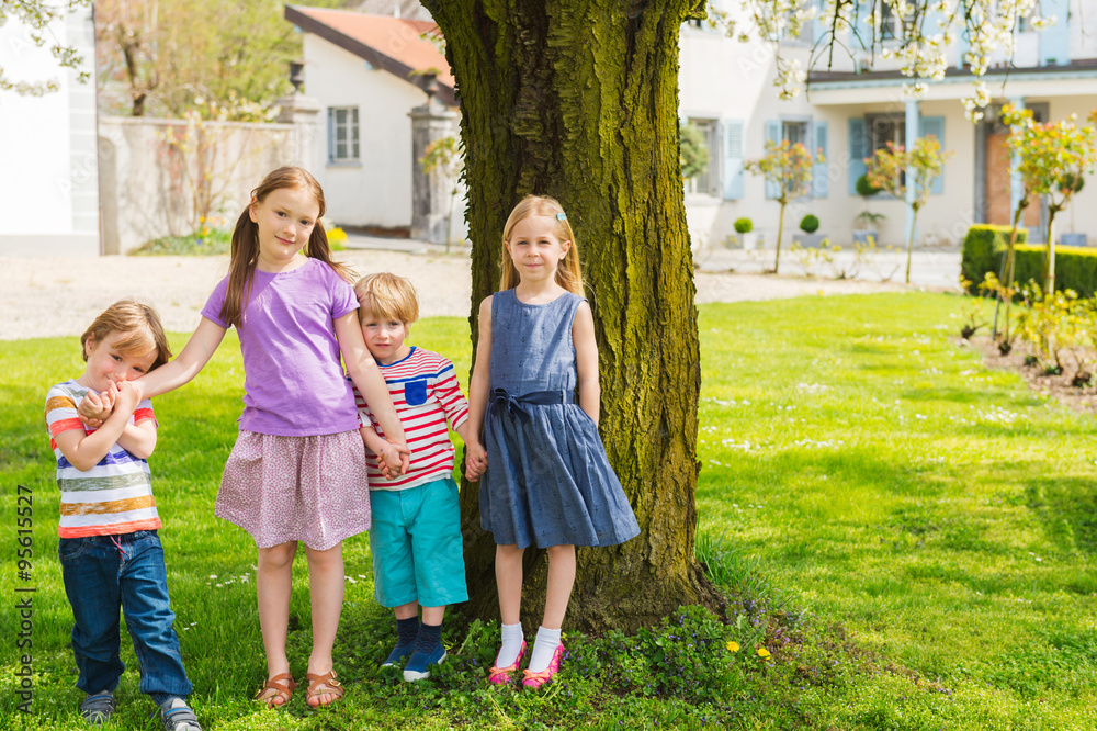 Outdoor portrait of 4 cute kids having fun outdoors, playing in a garden on a nice sunny day