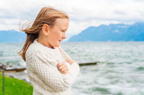 Fotografie Cute little girl of 8 years old playing by the lake on a very windy day, wearing