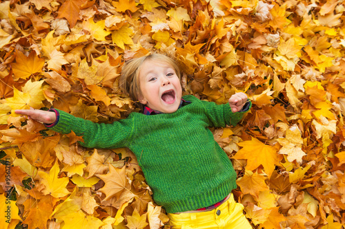 Autumn portrait of a cute little boy of 4 years old  playing with yellow leaves in the park  wearing green pullover