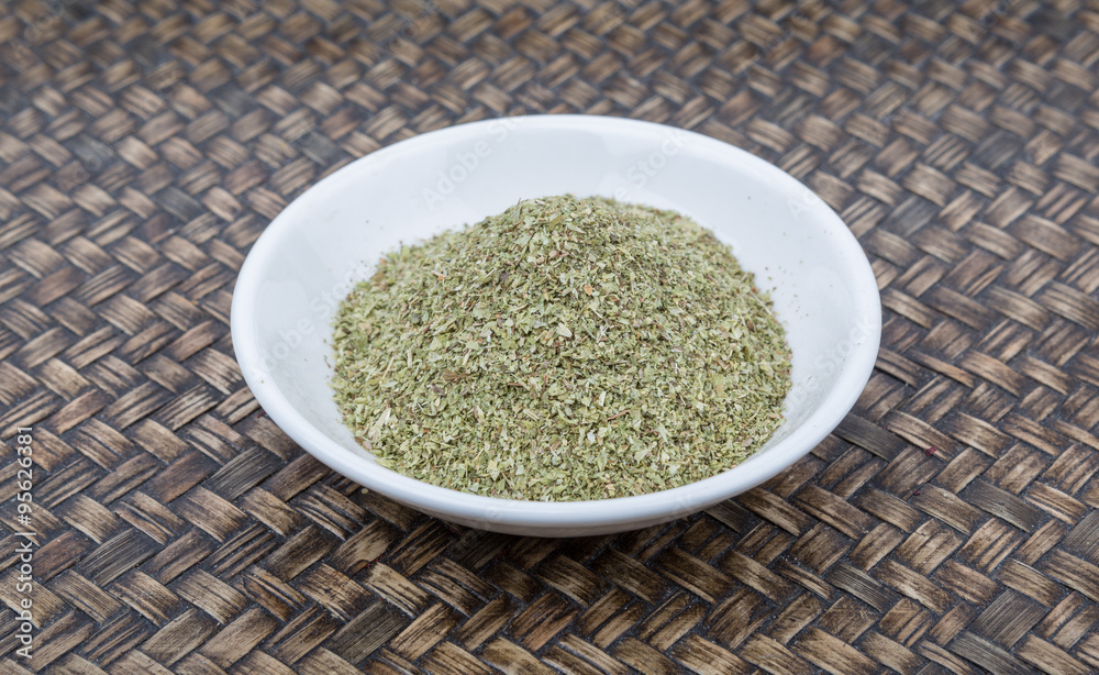 Dried oregano herbs in white bowl over wicker background Dried oregano herbs in white bowl over wicker background