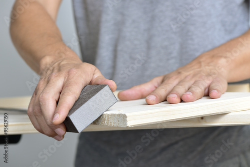 фотографія young man sanding a wooden board with a sanding block