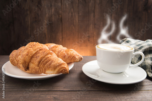 Breakfast coffee cup and croissant on wooden background