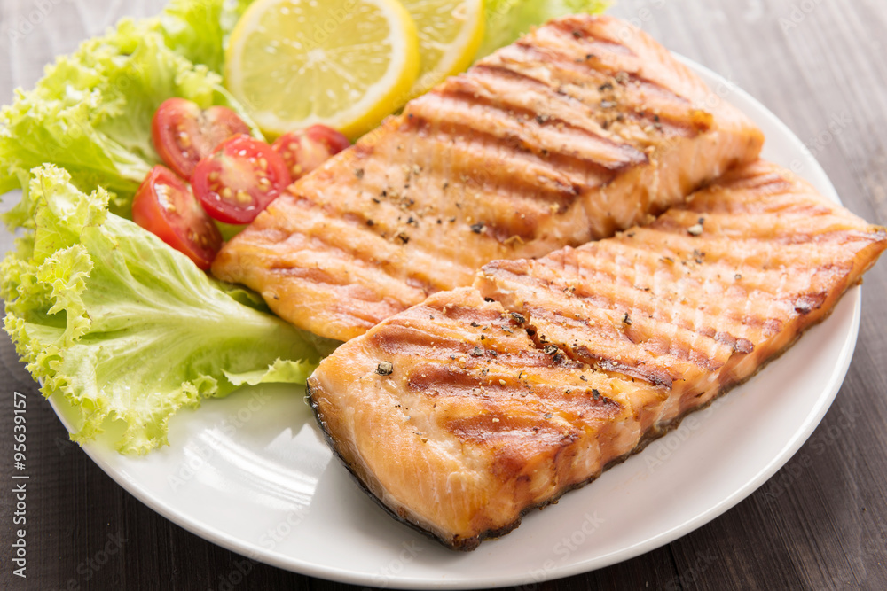 Grilled salmon with lemon,tomato on the wooden table Grilled salmon with lemon,tomato on the wooden table