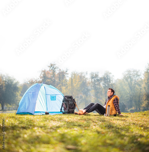 Relaxed hiker sitting next to a blue tent