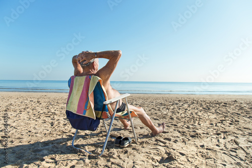 Old man sunbathing at the beach photo