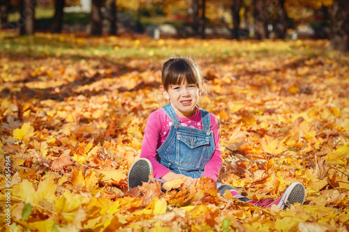 Happy little girl smiling while sitting on a pile of yellow autumn leaves 