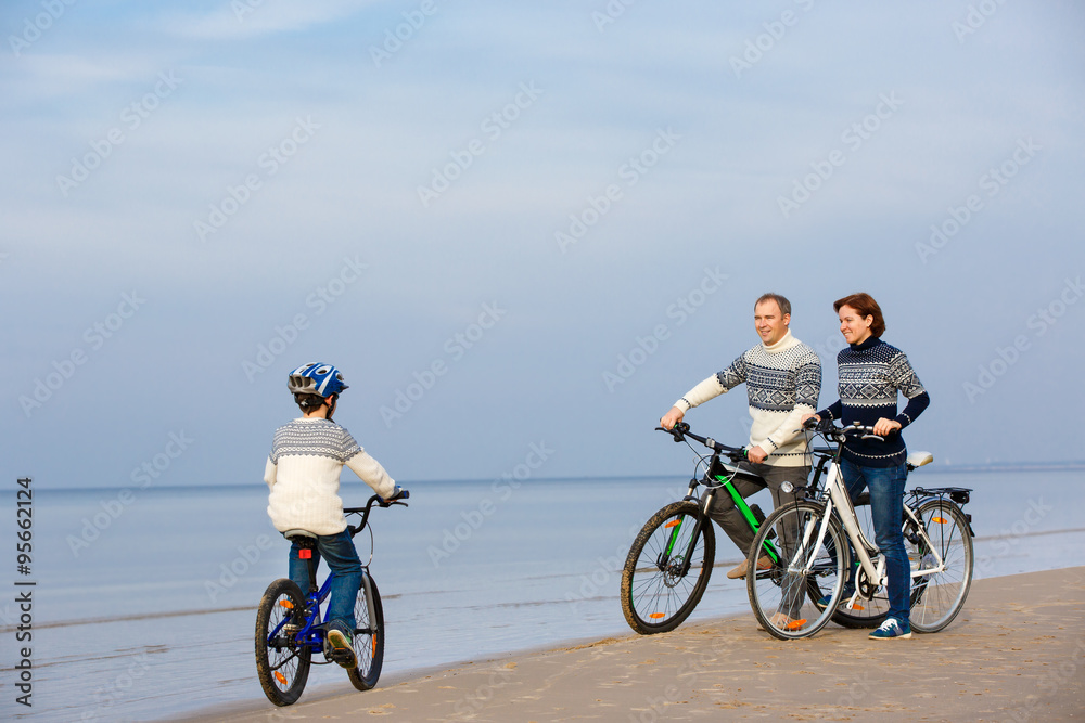 Naklejka premium Young family of three riding bicycles on beach