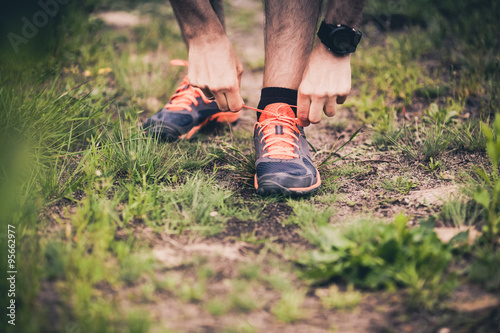Runner tying sports shoe on trail